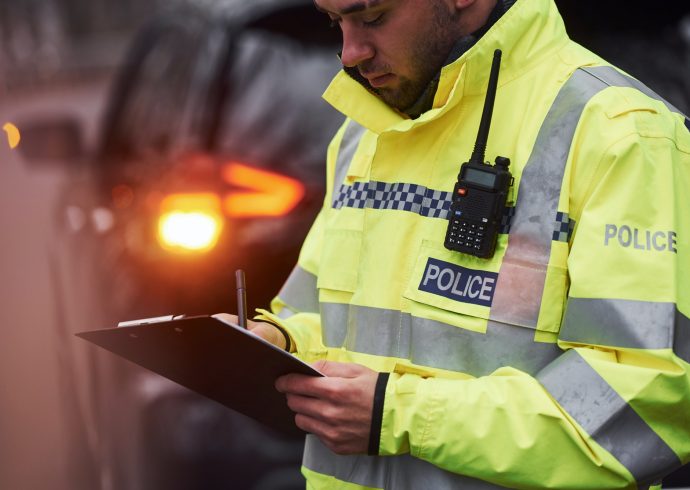 male-police-officer-in-green-uniform-standing-with-notepad-near-car.jpg